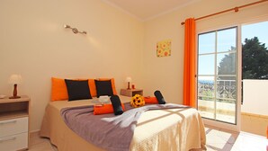 A bedroom with a bed, a nightstand, a window with curtains, and a view of the outdoors. - Villa Bella Vista (Albufeira)