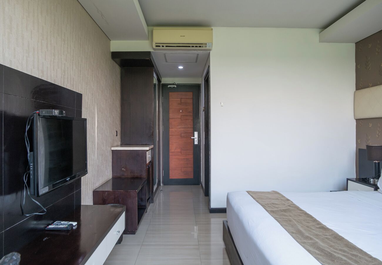 A hotel room with a bed, a TV, a desk, and a wooden door.