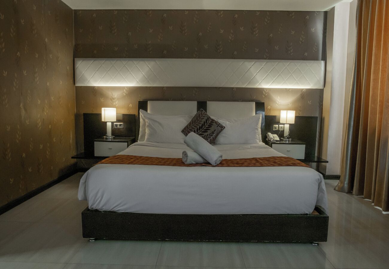 A large bed with a headboard, two bedside tables with lamps, and a brown patterned wall.