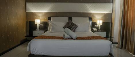 A large bed with a headboard, two bedside tables with lamps, and a brown patterned wall.