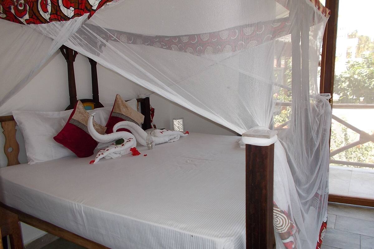 Una cama con dosel blanco, cabecera de madera y múltiples almohadas.