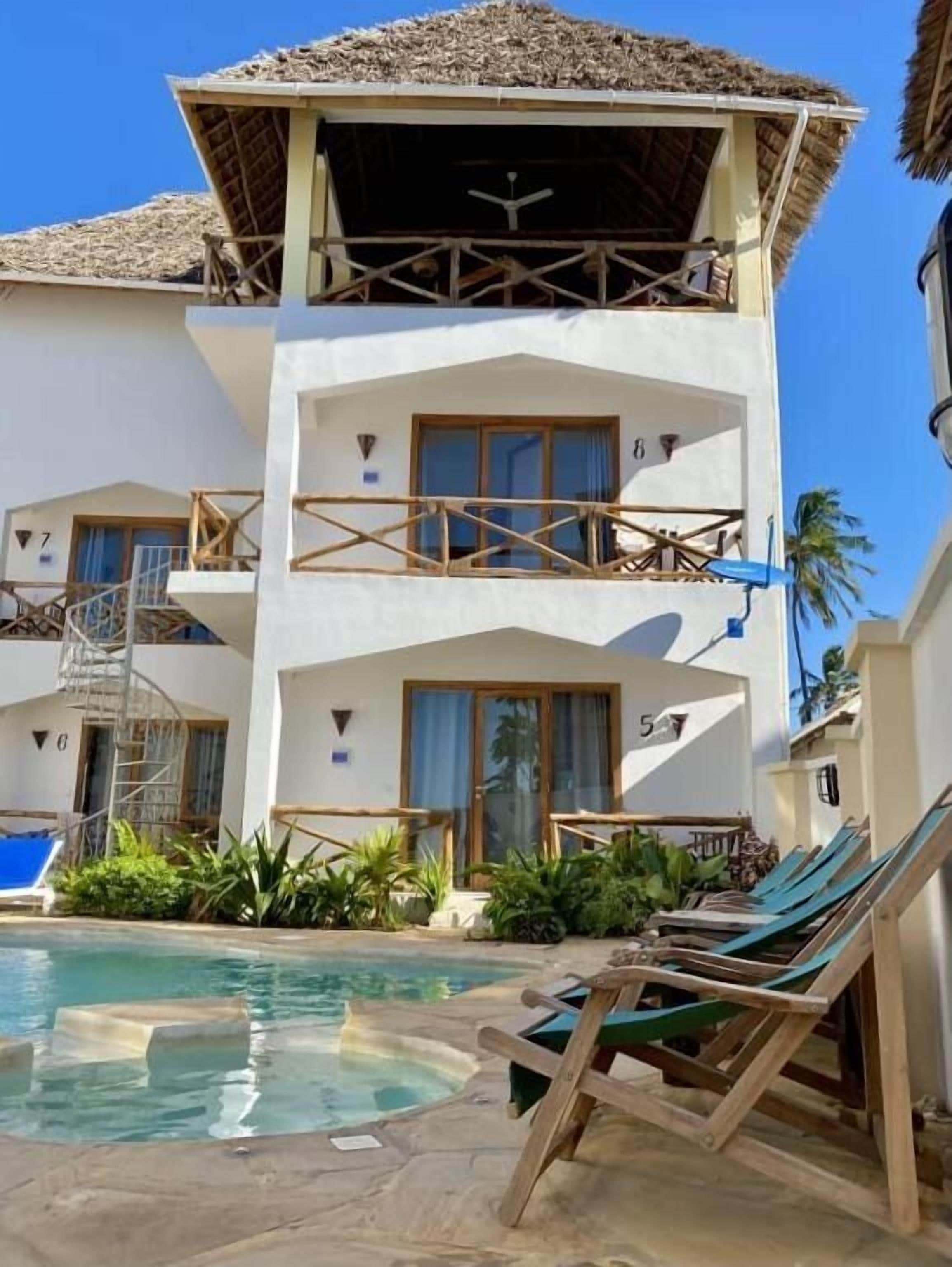 A multi-story hotel with a pool area, including lounge chairs and a hot tub.