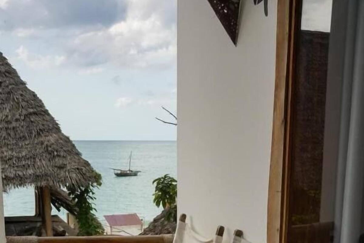 Una terraza de madera con vista al mar, un paraguas de paja y una silla de mimbre con cojín.