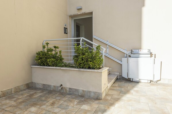 A building entrance with a metal staircase, a small planter with green shrubs, and a white utility box. - Pindemonte Garden by MMega (Florence)