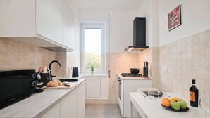 Une cuisine moderne avec des meubles blancs, un micro-ondes noir, une cuisinière et une fenêtre qui laisse entrer la lumière naturelle.