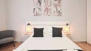 Une chambre d’hôtel moderne avec un grand lit, deux tables de chevet avec des lampes, un fauteuil gris et des œuvres d’art abstraites accrochées au mur.
