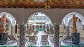 A spacious indoor area with a central pool, surrounded by white arches and patterned columns.