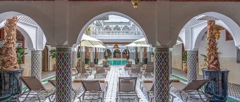 A spacious indoor area with a central pool, surrounded by white arches and patterned columns.