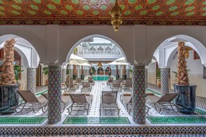 A spacious indoor area with a central pool, surrounded by white arches and patterned columns.