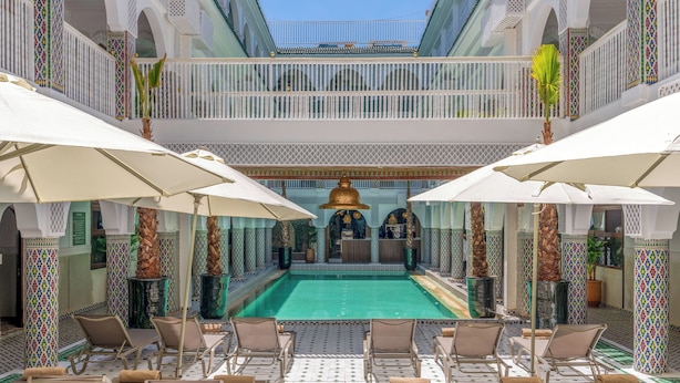 A poolside area with lounge chairs and umbrellas, a central pool, and a decorative fountain.