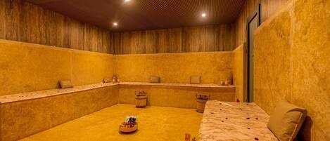 Un cuarto de spa con techo de madera, una cama de mármol y un balde de madera con una botella.