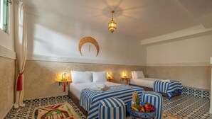 A hotel room with two beds, a decorative wall hanging, a patterned rug, and a fruit bowl on the floor.