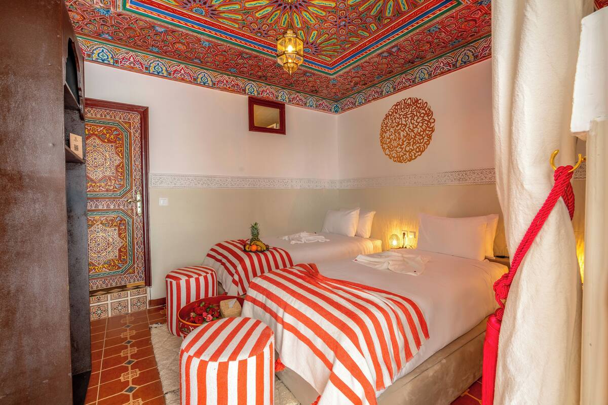 A hotel room with a large bed, two bedside tables, a decorative ceiling, and a patterned wall.