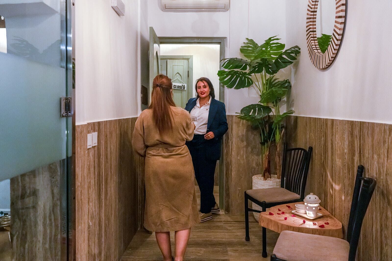 A hallway with a closed door, a potted plant, and a table with a vase and a candle.