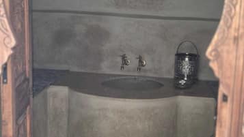 Un baño pequeño y cerrado con un lavamanos y un recipiente de metal.