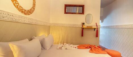 A hotel room with a bed, pillows, a bedside table with a mirror, and a decorative wall pattern.
