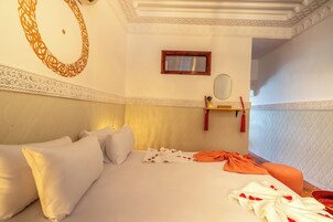 Una habitación de hotel con una cama, almohadas, una mesita de noche con espejo y un diseño decorativo en la pared.