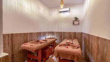 A spa room with two massage tables, each covered with a towel and a bottle of oil.
