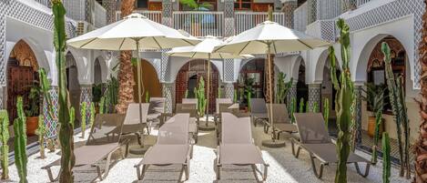 Une cour intérieure agrémentée d’arcades blanches, de chaises longues et de parasols.