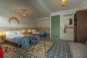 A hotel room with two beds, a sofa, a small table with fruit, patterned rugs, and decorative wall sconces.