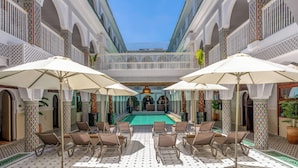 A poolside area with lounge chairs and umbrellas, a central pool, and ornate architectural details. - Palais Moulay Said & SPA (Marrakech)