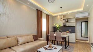 Una sala de estar moderna con un sofá color beige, un comedor con mesa y sillas, y una cocina con horno empotrado y armarios.