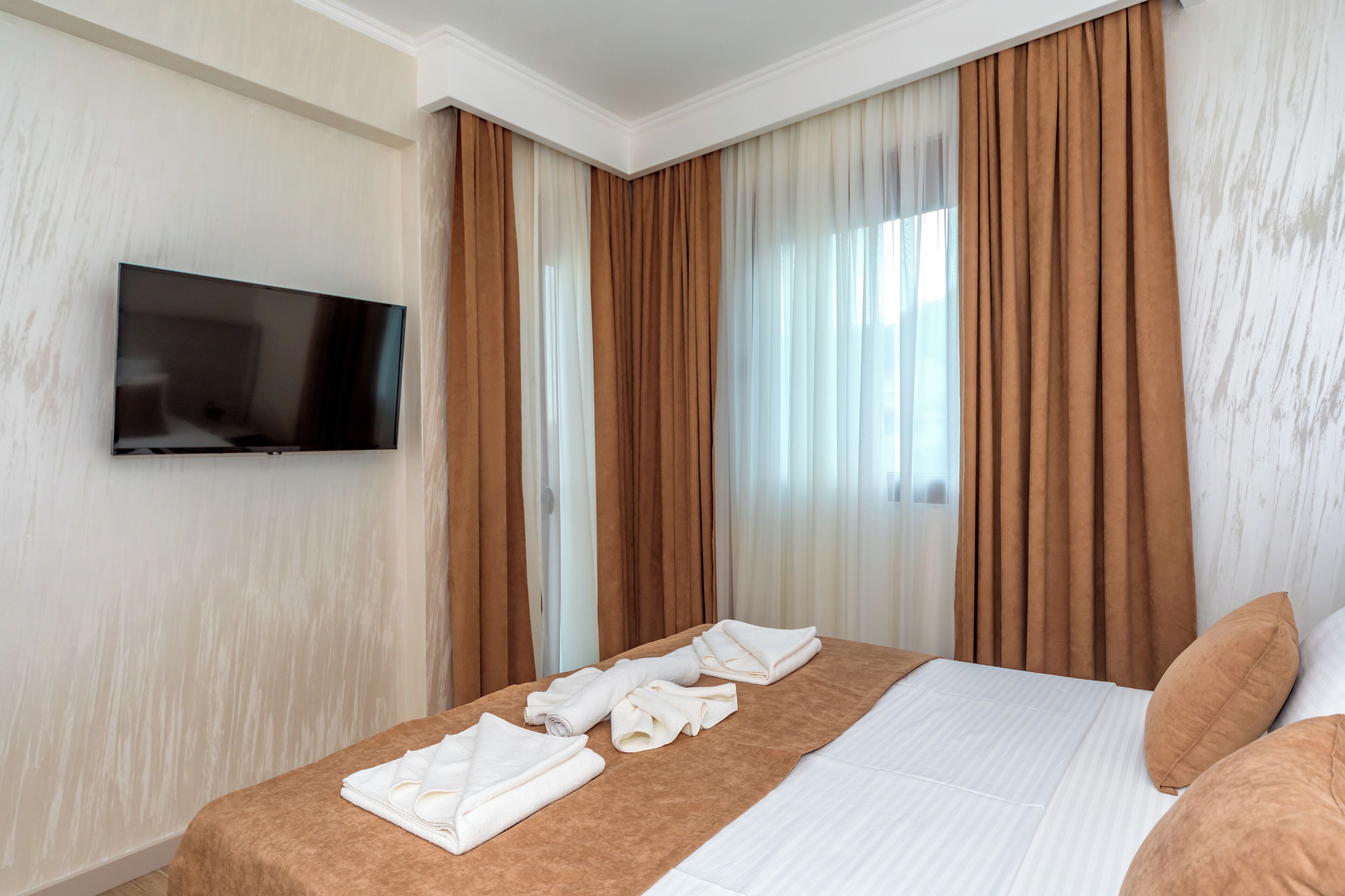 Una habitación de hotel con una cama, un televisor de pantalla plana montado en la pared y un ventanal con cortinas marrones.