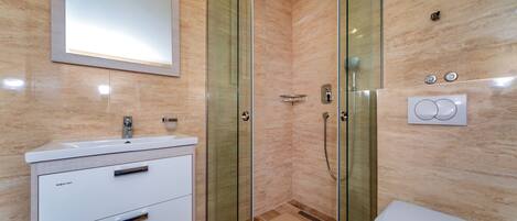 A modern bathroom with a glass-enclosed shower, a white sink, and a toilet.