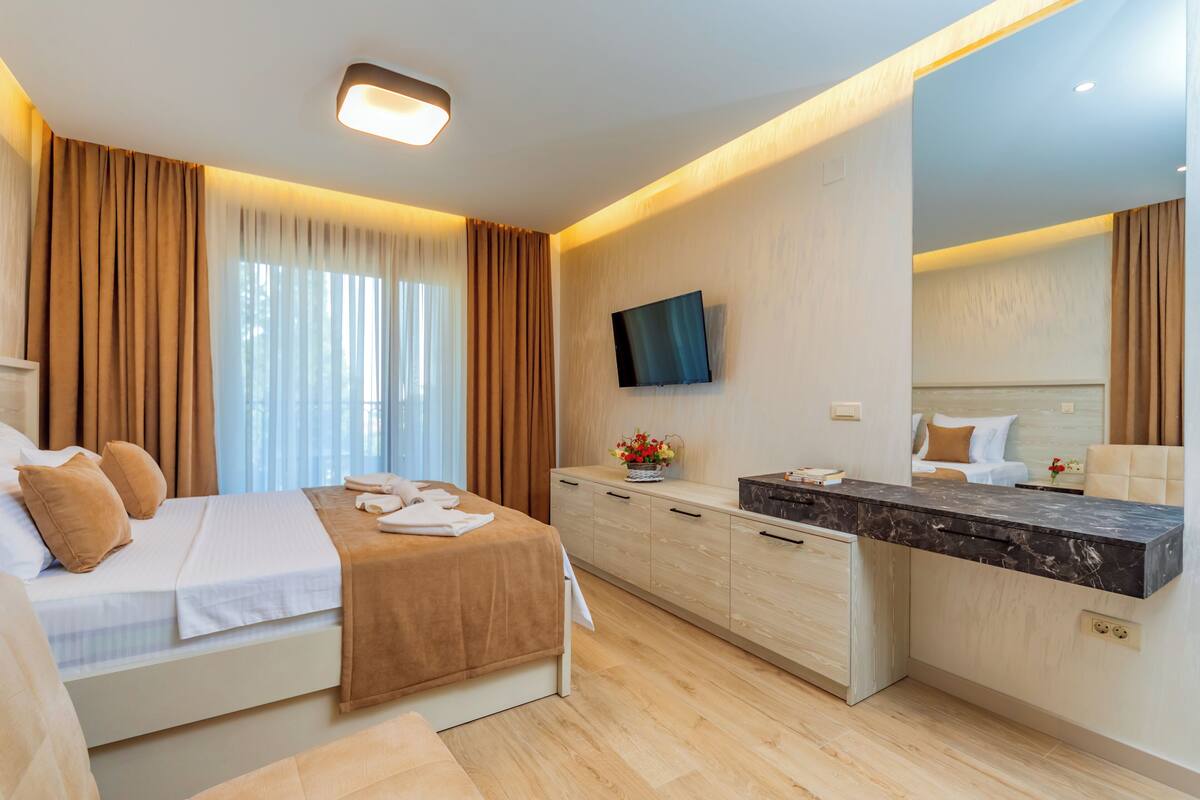 A modern hotel room with a bed, a desk, a flat-screen TV, and a large mirror.