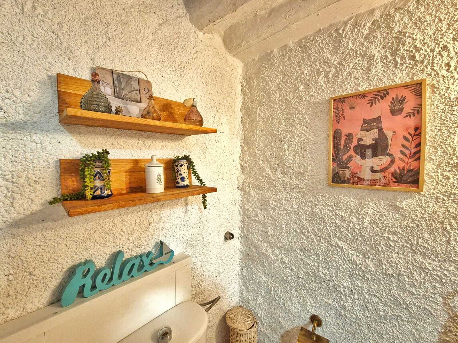 Un baño rústico con pared texturizada, estantes de madera con adornos, una obra de arte enmarco y un cartel que dice 'Relax'.