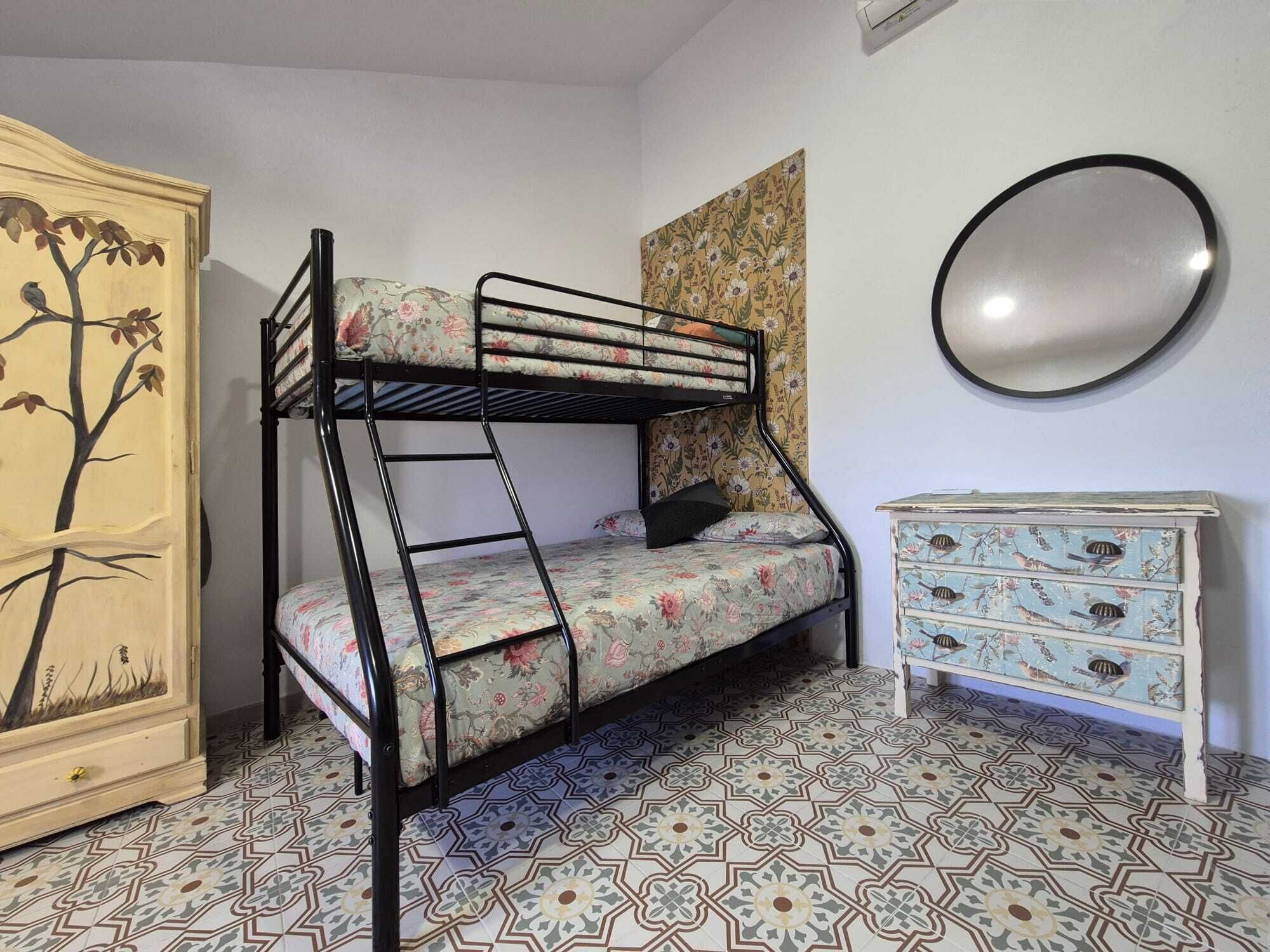 Una cama litera con ropa de cama floral, un aparador con diseños de pájaros y baldosas de suelo estampadas.