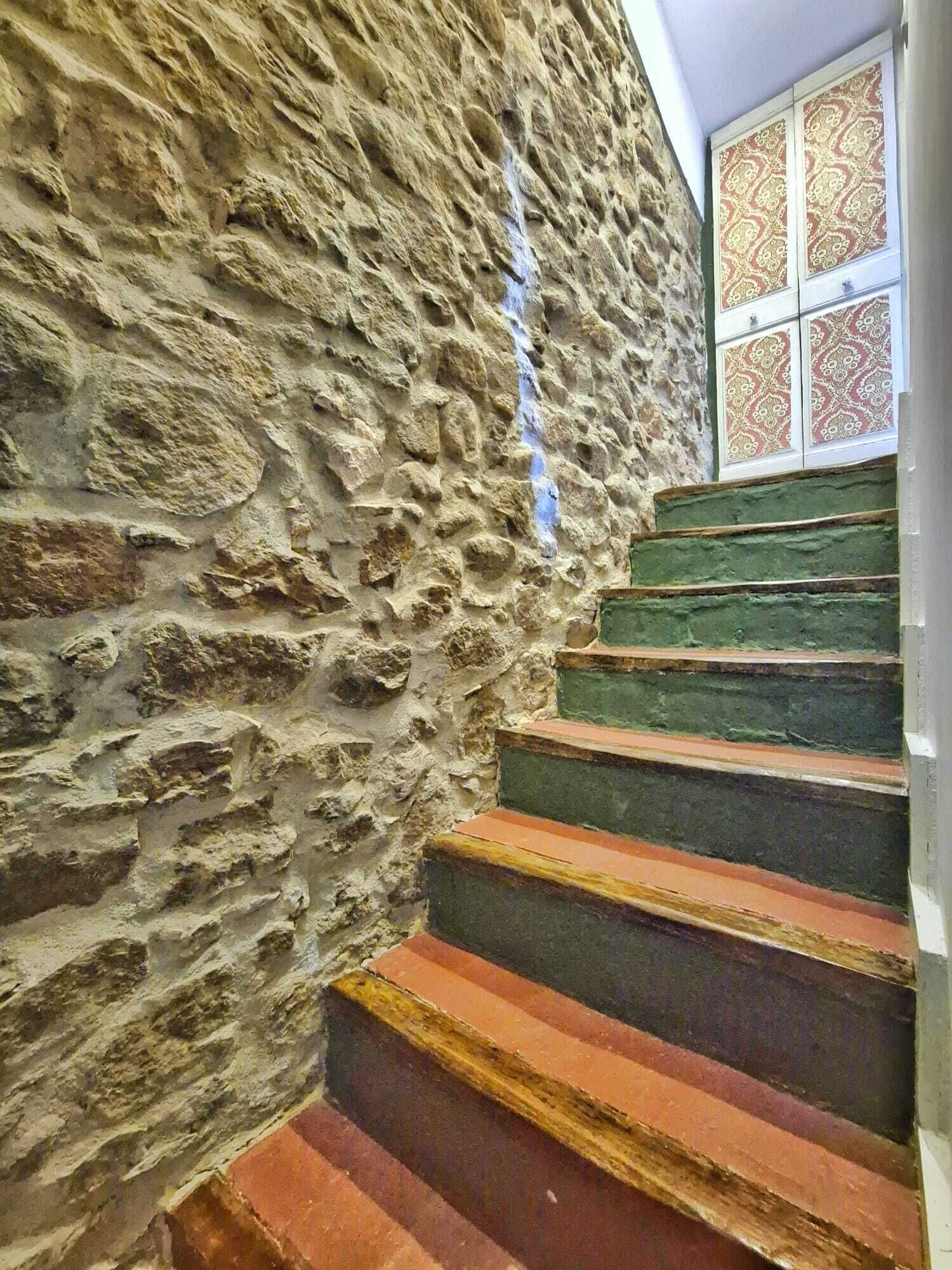 Un muro in pietra con una stretta scala che conduce a una finestra decorata.