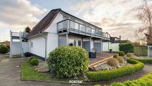 Une maison moderne à deux étages, dotée d’un balcon, d’un jardin bien entretenu et d’une allée d’accès fermée par un portail.