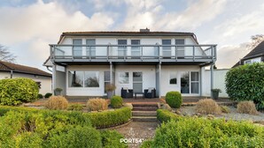 Une maison à deux étages dotée d’un balcon, d’un porche et d’un jardin bien entretenu.
