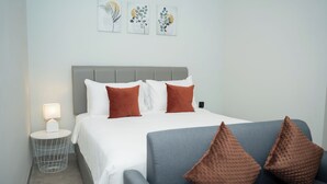 A neatly arranged bedroom with a bed, a side table with a lamp, and a sofa with decorative pillows. - Studio 27 Sanur - Self Check-in (Denpasar)