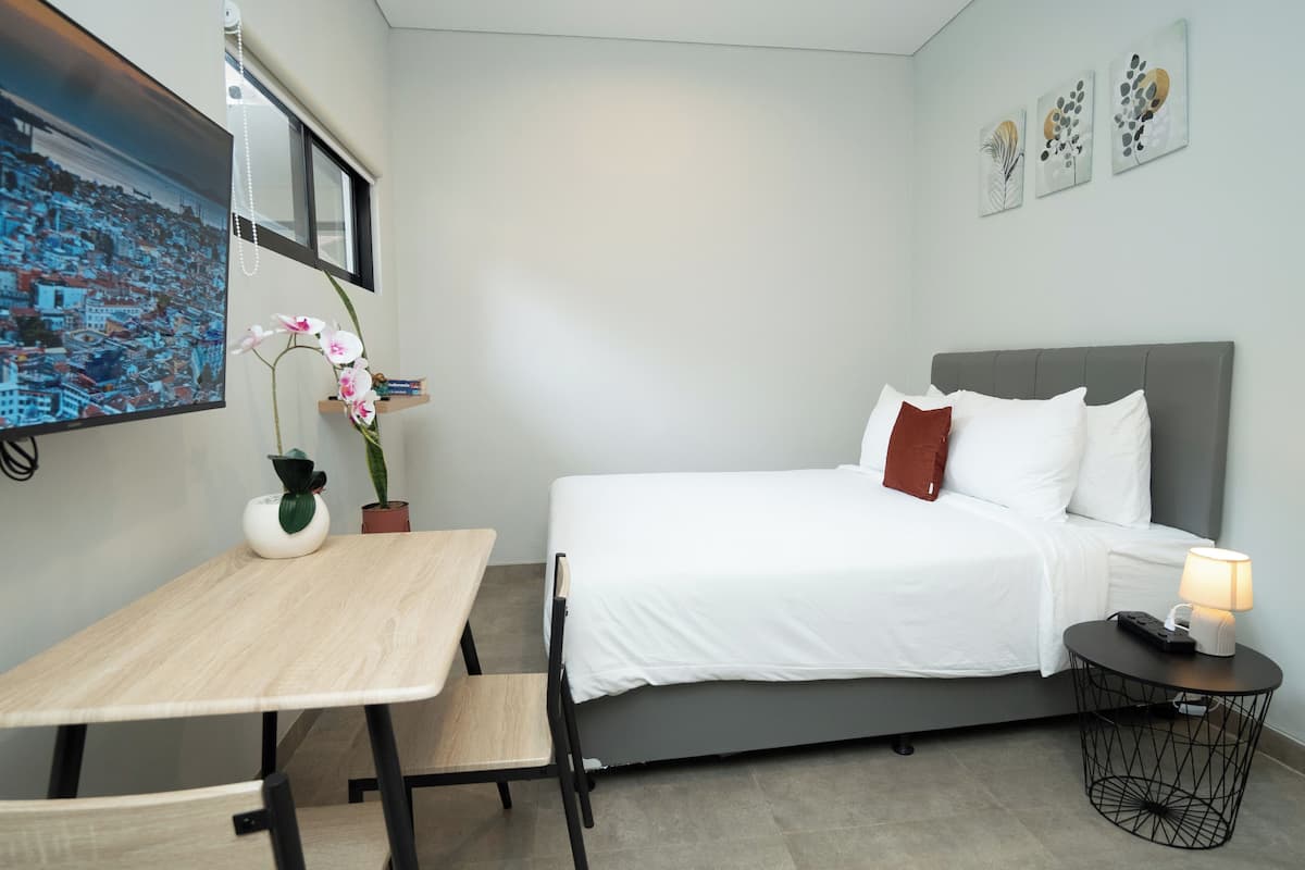 Een netjes ingerichte hotelkamer met een bed, nachtkastje, lamp en een bureau met stoelen.