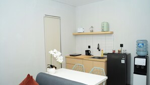 A compact kitchen with a refrigerator, a water dispenser, a coffee maker, and a small countertop. - Studio 27 Sanur - Self Check-in (Denpasar)