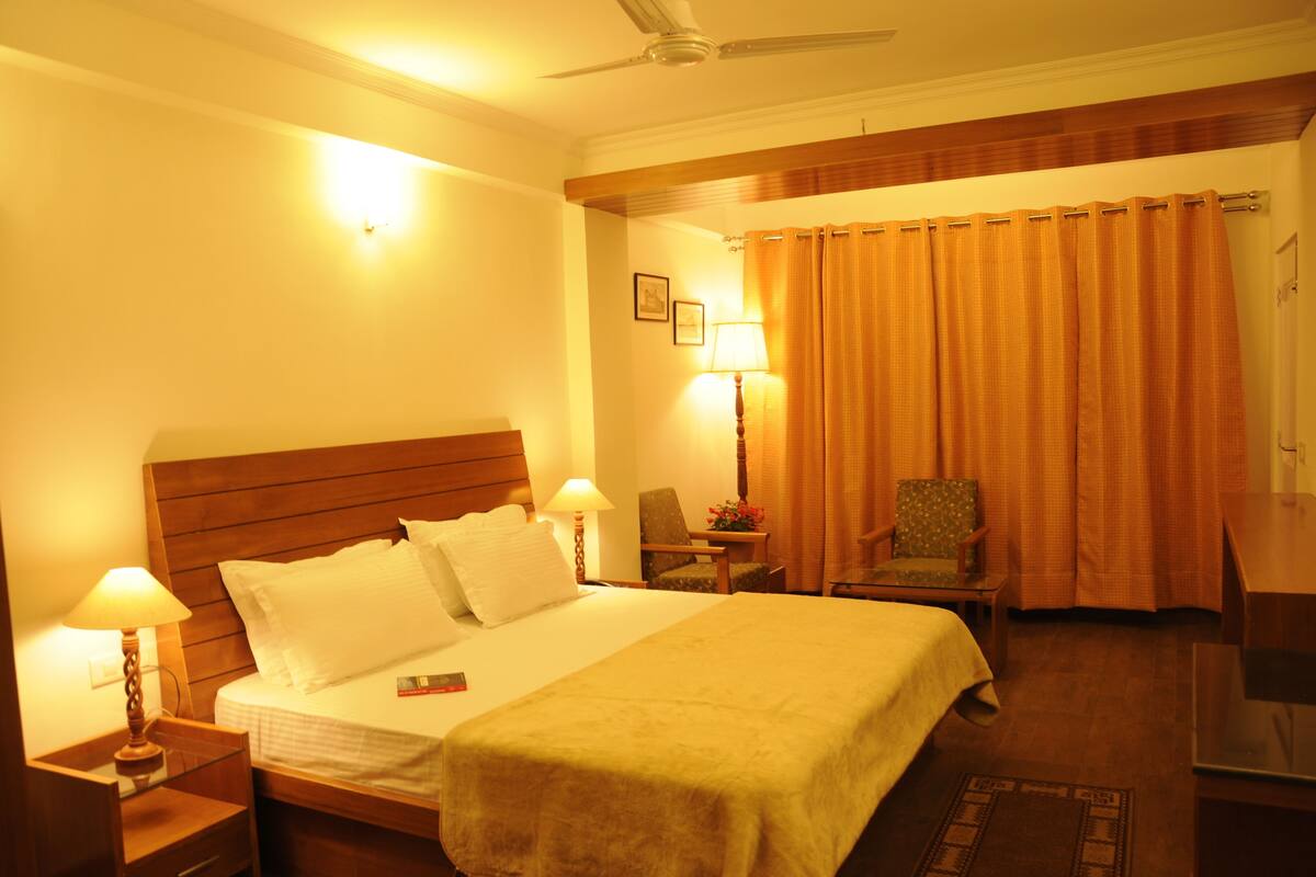 A hotel room with a bed, bedside lamps, a chair, a desk, and a curtain.