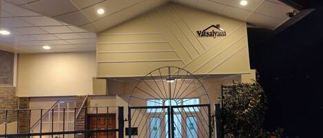 Egy szálloda bejárata, melyhez egy kapuval ellátott felhajtó vezet, emellett található itt egy lépcsőház, és egy „Vatsalya” felirattal ellátott tábla.