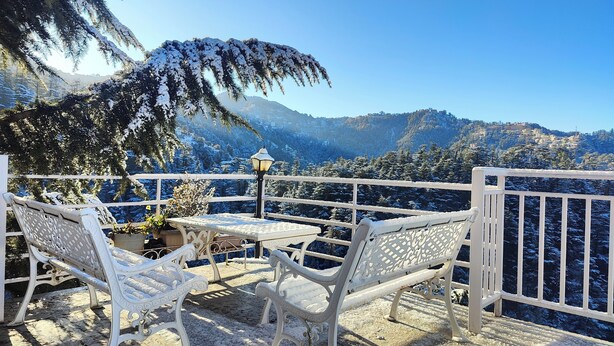 A snow-covered outdoor seating area with a table and chairs, overlooking a mountainous landscape. - Vatsalyam Homestay (Shimla)
