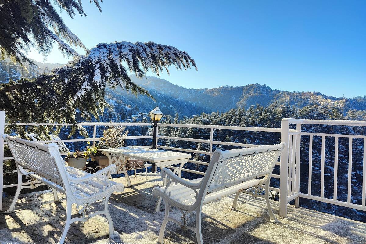A snow-covered outdoor seating area with a table and chairs, overlooking a mountainous landscape.
