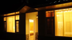A hotel room with a bed, a nightstand, and a window with curtains. - Vatsalyam Homestay (Shimla)