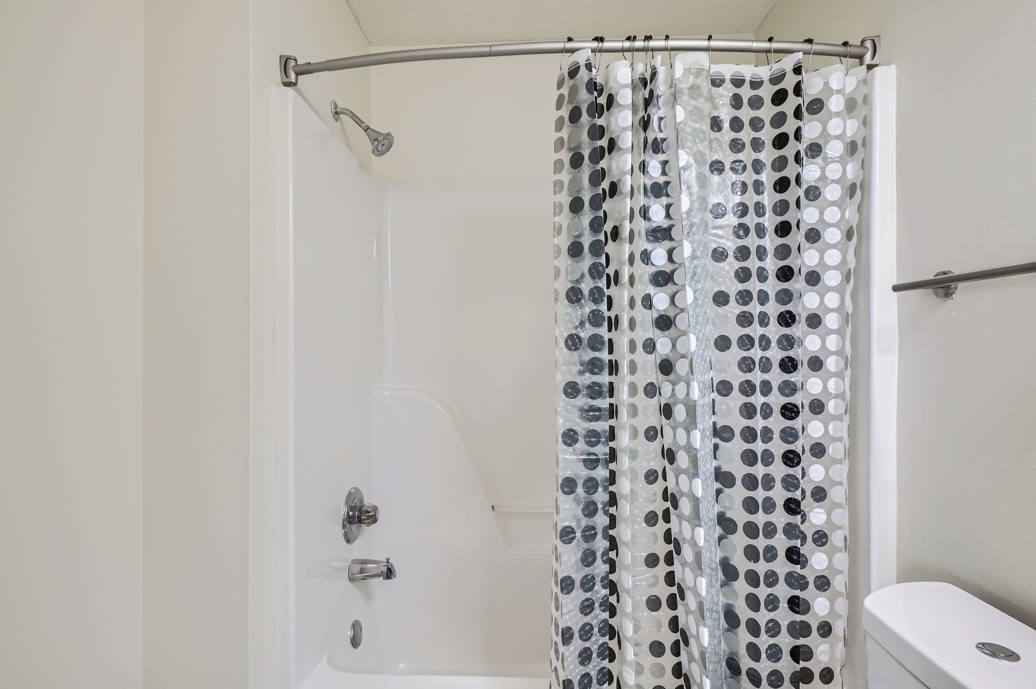 A shower area with a curved showerhead, a white bathtub, and a polka dot shower curtain.