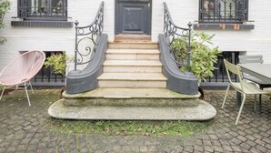 Ein weißes Gebäude mit einer schwarzen Tür, einer überdachten Treppe und einem Ziegelhof.