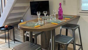 A dining area with a wooden table, four metal stools, and a TV mounted on the wall. - Le Cocon de la Garrigue (Agde)