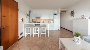 A compact kitchen with white cabinets, a central island with stools, a small refrigerator, and a decorative plant. - Casa Azzurra Seaview Addaura by Wonderful Italy (Palermo)