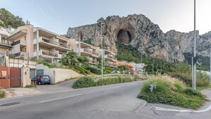 A coastal road with a mountain backdrop, a gated entrance, and a blue car parked by the side. - Casa Azzurra Seaview Addaura by Wonderful Italy (Palermo)