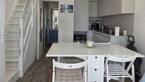 Una cocina compacta con armarios blancos, una mesa de comedor con dos sillas y un microondas.