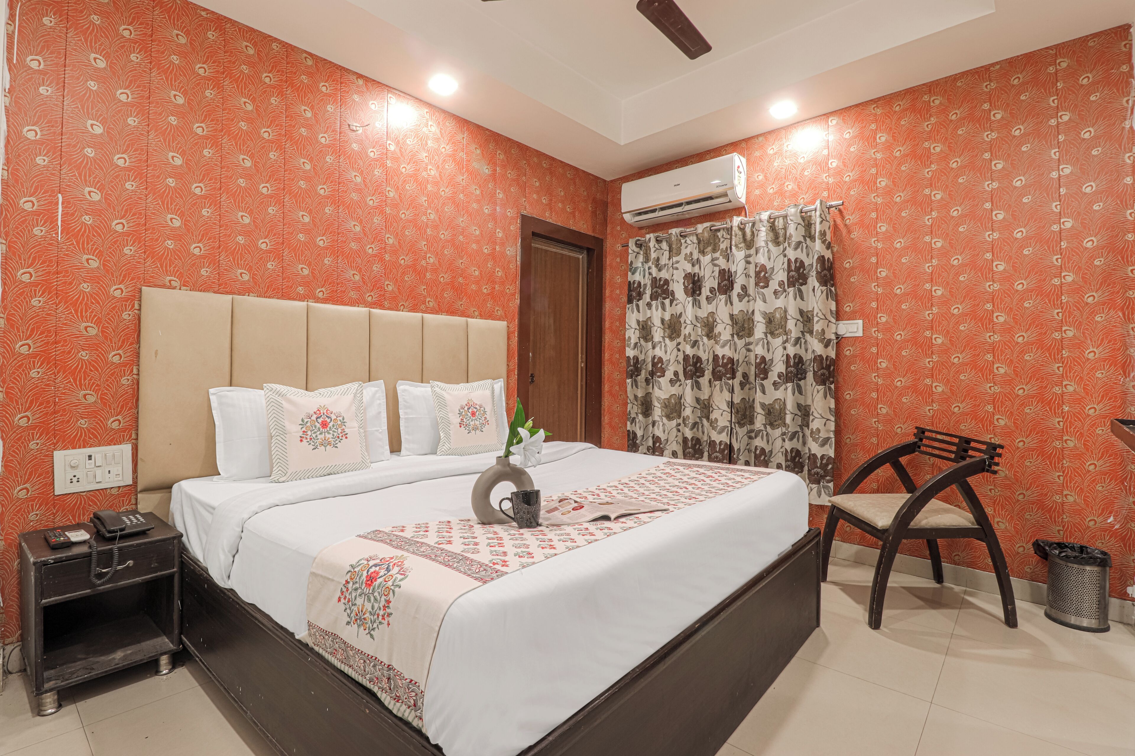 A bedroom with a bed, bedside table, chair, and an air conditioning unit.