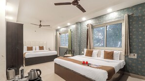 A hotel room with two beds, a ceiling fan, a window with curtains, a small table with a tray, and a wall with a decorative pattern. - Hotel Amishi (Haridwar)